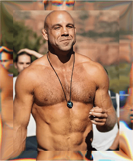Confident, shirtless man with a necklace, smiling outdoors during a fitness event.